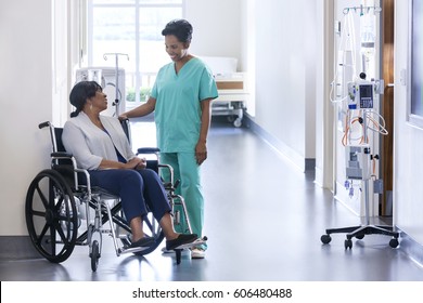 African American Nurse In Scrubs With Patient In Hospital Wheelchair In Corridor Of Specialist Care Clinic