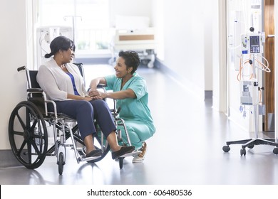 African American Nurse In Scrubs With Patient In Hospital Wheelchair In Corridor Of Specialist Care Clinic