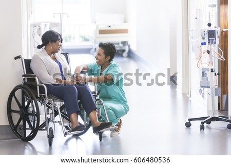 African American nurse in scrubs with patient in hospital wheelchair in corridor of specialist care clinic