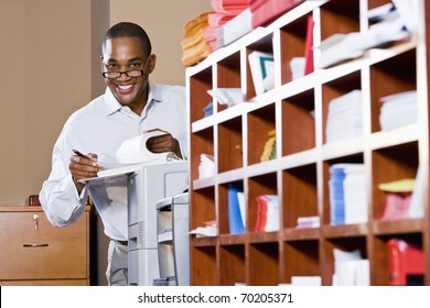 African American Office Worker Reviewing Document Binder, Leaning On Printer In Mailroom