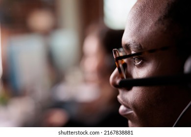 African american operator listening to client on helpline call, using customer service network on headset. Male receptionist working at call center telemarketing assistance. Close up.