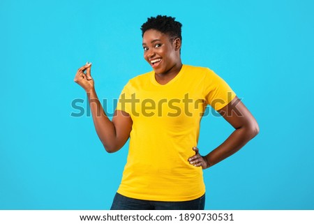 African American Oversized Woman Gesturing Clicking Fingers Standing Posing On Blue Background In Studio, Smiling To Camera. Finger Snap Gesture Concept