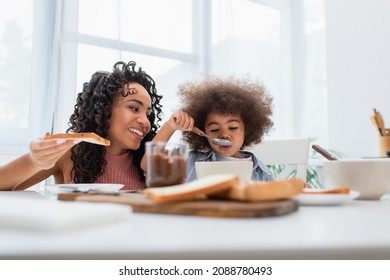 African American Parent Holding Bread While Daughter Eating Cereal At Home