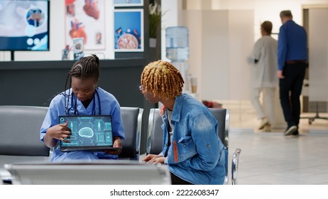 African American Patient Analyzing Brain Neurology Scan At Medical Consultation In Reception Lobby With Nurse. Woman And Assistant Looking At Tomography And Neural System Diagnosis On Laptop.