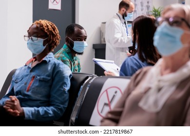 African American Patient Attended By Female Doctor. Different Ethnicities, Ages People Wearing Masks Preventing Covid 19 Spread At Doctor Office Reception Area, General Shot Of Hospital Waiting Room.