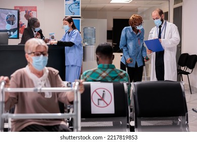 African American Patient In Crutches At Hospital Lobby, Talking To Male Doctor About Healthcare And Recovery. Woman With Chronic Disability And Impairment Doing On Toutine Checkup Visit.