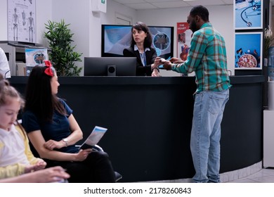 African American Patient At Hospital Front Desk Paying At Pos Using Credit Card For Medical Services At Clinic. Man After Doctor Appointment Typing Pin Number After Making Transaction For Healthcare.