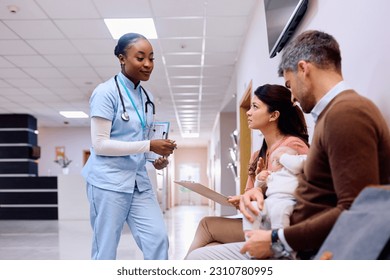 African American pediatric nurse assisting parents with baby to fill out medical data in waiting room at the clinic.  - Powered by Shutterstock