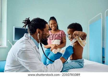 African American pediatrician examining a happy boy with stethoscope at doctor's office.