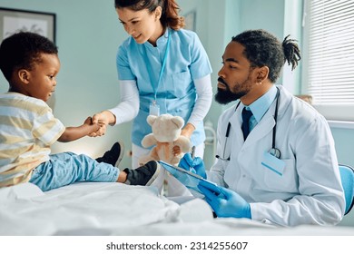 African American pediatrician taking notes while nurse and little boy are shaking hands at the clinic.  - Powered by Shutterstock