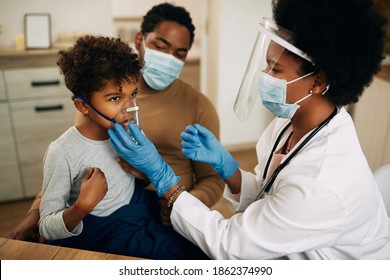 African American Pediatrician Using Nebulizer During Inhaling Therapy Of A Small Boy Due To Coronavirus Pandemic. 