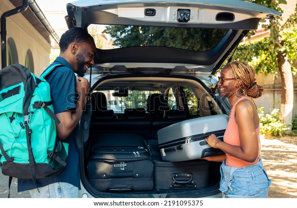 African\
american people loading baggage in automobile to leave on holiday\
vacation trip. Partners travelling by car with luggage, suitcase\
and bags to go to summer adventure\
cityscape.
