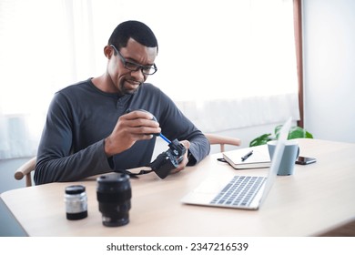 African American photographer cleaning camera lens and professional camera while sitting in the home office. Freelance photographer online marketing. Startup small business owner entrepreneur Concept. - Powered by Shutterstock