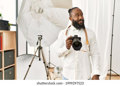 African american photographer man working at photography studio smiling looking to the side and staring away thinking. 
