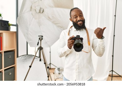 African american photographer man working at photography studio pointing to the back behind with hand and thumbs up, smiling confident 