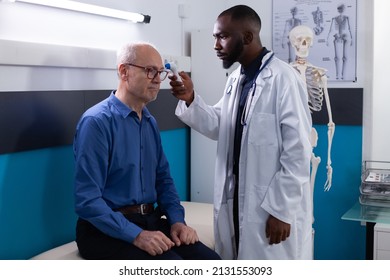 African american physician doctor putting infrared thermometer on senior man patient foredhead measuring temperature hospital office. Therpist explaining flu symtptoms during medical consultation in - Powered by Shutterstock