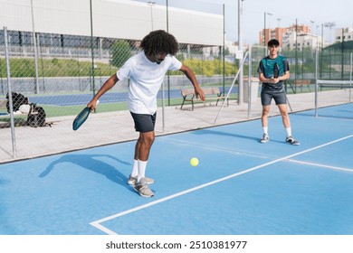 An African American pickleball player in action, hitting the ball on a blue court, with another player observing. Concept of athleticism and focus. - Powered by Shutterstock