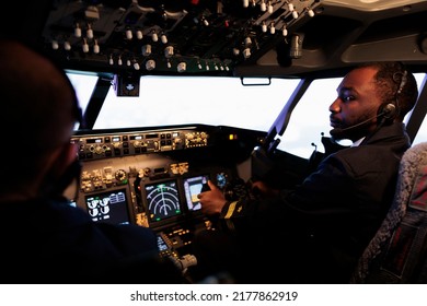 African american pilot flying aircraft jet doing teamwork with captain, using dashboard command and navigation. Team of airliners pushing control panel buttons and lever to takeoff and fly. - Powered by Shutterstock