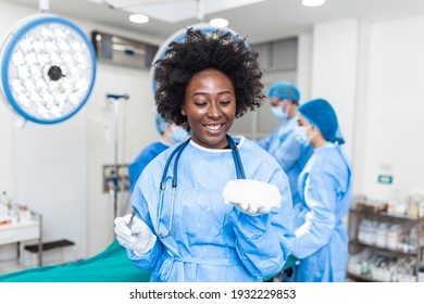 African American Plastic surgeon woman holding silicon breast implants in surgery room interior. Cosmetic surgery concept - Shutterstock ID 1932229853