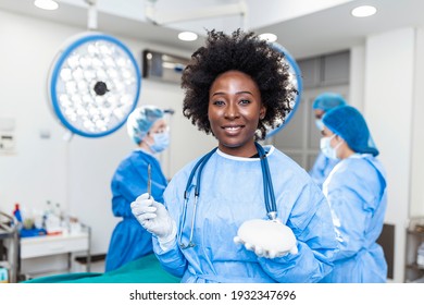 African American Plastic Surgeon Woman Holding Silicon Breast Implants In Surgery Room Interior. Cosmetic Surgery Concept