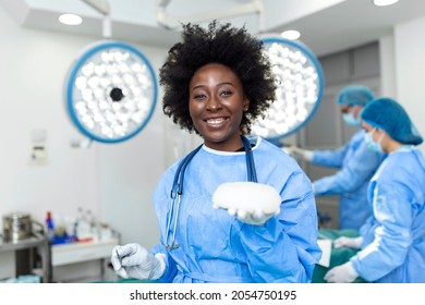 African American Plastic Surgeon Woman Holding Silicon Breast Implants In Surgery Room Interior. Cosmetic Surgery Concept