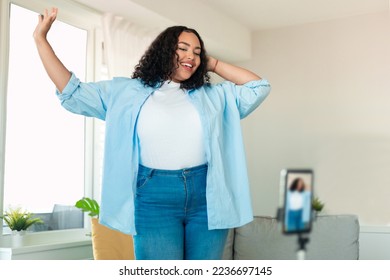 African american plus size female influencer recording video on smartphone, dancing on camera at home. Positive lifestyle blogger making content for her blog, filming for social media - Powered by Shutterstock