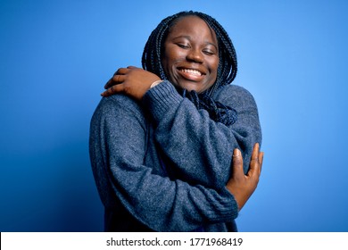African american plus size woman with braids wearing casual sweater over blue background Hugging oneself happy and positive, smiling confident. Self love and self care