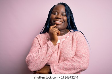 African american plus size woman with braids wearing casual sweater over pink background looking confident at the camera with smile with crossed arms and hand raised on chin. Thinking positive. - Powered by Shutterstock