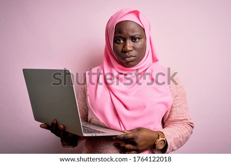 African american plus size woman wearing muslim hijab using laptop over pink background skeptic and nervous, frowning upset because of problem. Negative person.