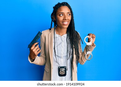 African American Police Woman Holding Gun And Handcuffs Smiling Looking To The Side And Staring Away Thinking. 