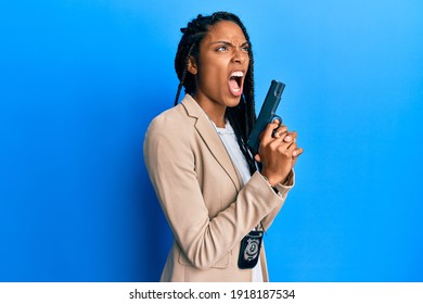 African American Police Woman Holding Gun Angry And Mad Screaming Frustrated And Furious, Shouting With Anger. Rage And Aggressive Concept. 