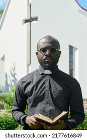 African American Preacher In Black Shirt With White Clerical Collar Holding Holy Bible While Reading Verses From Old Or New Testament