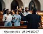 African american preacher is leading her congregation in prayer, with their hands raised in worship. They are all gathered together in the church pews