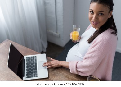 African American Pregnant Woman With Orange Juice Using Laptop