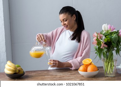 African American Pregnant Woman Pouring Juice At Kitchen With Fresh Fruits