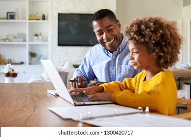 African American pre-teen girl sitting at a table in the dining room working on a laptop computer watched by her home tutor, close up, selective focus