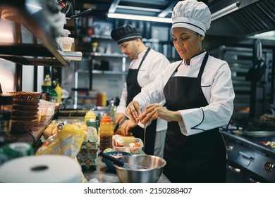 African American professional cook cracking an egg while preparing meal with her coworker in the kitchen at restaurant.  - Powered by Shutterstock