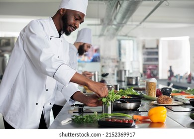 African American Professional Head Chef Picking Fresh Green Herbs To Improve Gourmet Dish Taste. Male Cook Wearing Cooking Uniform Preparing Organic Meal While In Restaurant Kitchen.