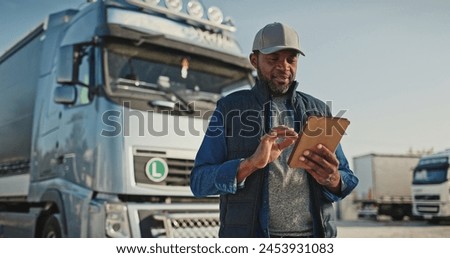 African American professional truck driver setting up navigation for destination. Checking his route on tablet computer and standing by long vehicle. Transportation service.