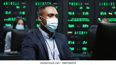 African American IT Programer Working On Desktop Computers In Data Center Control Room. Young Professional Writing On Sophisticated Programming Code Language Sitting In Mask At Workplace Data Storage