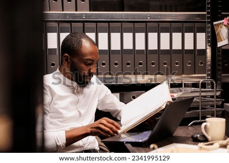 African american prosecutor reading file, preparing for case in police office with archival records. Law enforcement professional analyzing forensic expertise folder at night time