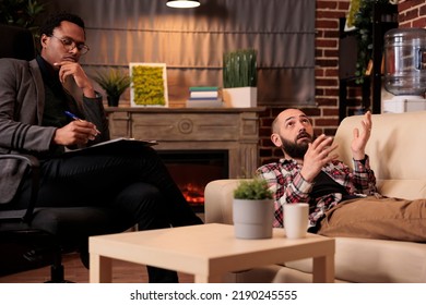 African American Psychologist Consulting Man Laying On Couch, Doing Psychoanalysis To Solve Problems At Therapy Session. Talking About Behavior Issues And Giving Counseling Advice.