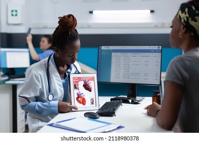 African American Radiologist Doctor Holding Tablet Explaining Heart Xray Discussing Medical Treatment With Sick Patient Woman During Clinical Appointment. Cardiologist Working In Hospital Office.