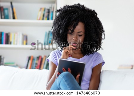 African american reading newspaper online with tablet computer indoors at home