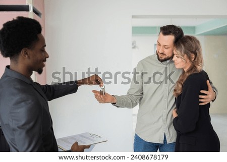 African american real estate wearing ellegant new suit holding keys from new home house in hands giving to new happy homeowners of the new building Stock photo © 