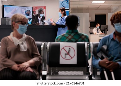 African American Receptionist Talking To Asian Nurse At Reception Desk In Hospital Lobby, Chatting About Healthcare Service And Medical Appointment. Facility Staff During Covid 19 Epidemic.