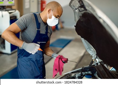 African American Repairman Wearing Protective Face Mask And Examining Car Oil In A Workshop. 