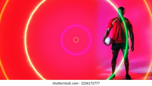 African american rugby player holding ball over colorful illuminated circles on pink background. Copy space, composite, pink, sport, competition, standing, shape and abstract concept. - Powered by Shutterstock