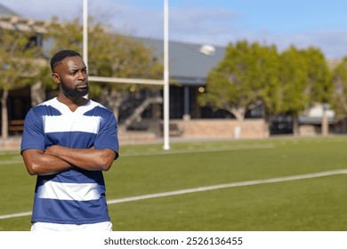 African american rugby player standing strong and fit on sports field, copy space. trees and a building are visible in background under a clear sky, unaltered - Powered by Shutterstock