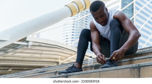 African American Runner Tying Shoelaces Of Sneaker With Water Bottle In Urban City Outdoors 